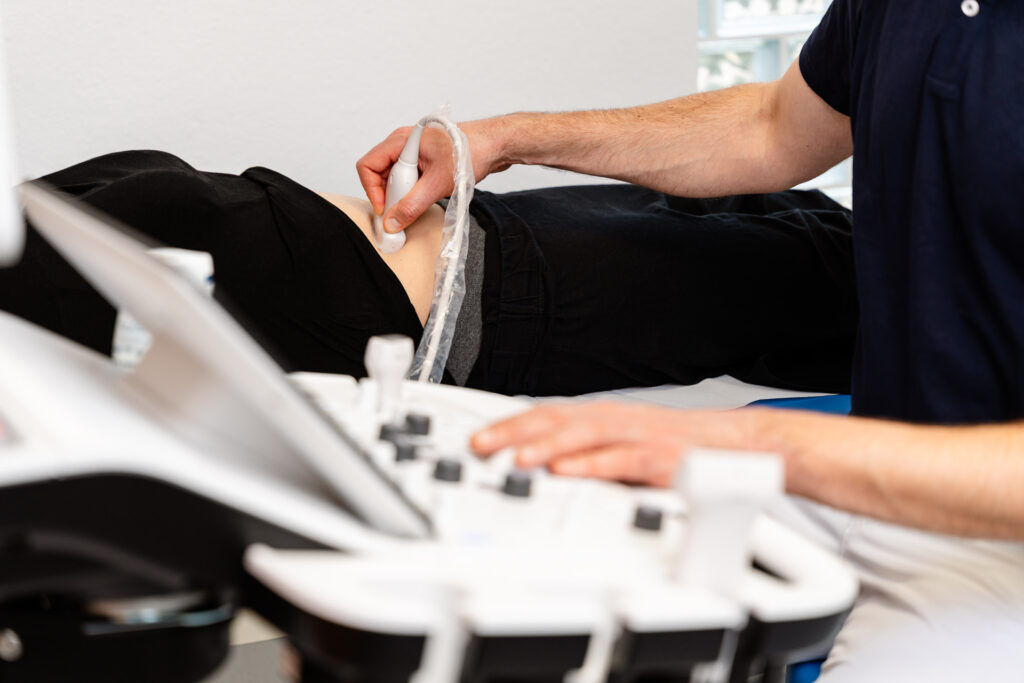 Tim Grüber führt eine Ultraschalluntersuchung des Abdomens einer Patientin durch. Moderne medizinische Technik im Einsatz zur Diagnose.